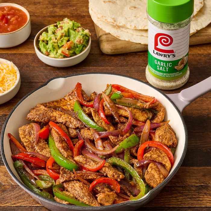 A skillet of chicken fajita ingredients with Lawry's Garlic Salt.
