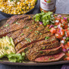 A plate of sliced carne asada with avocado pico de gallo and a container of Carne Asada Seasoning.