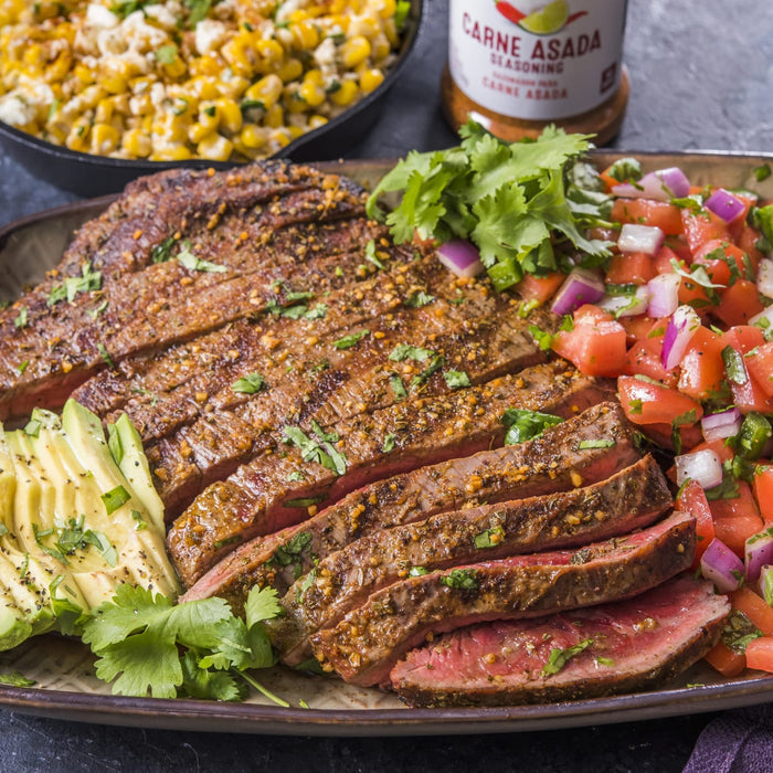 A plate of sliced carne asada with avocado pico de gallo and a container of Carne Asada Seasoning.