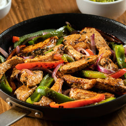 A skillet filled with sizzling chicken fajitas, featuring colorful bell peppers and red onions.