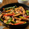 A skillet filled with sizzling chicken fajitas, featuring colorful bell peppers and red onions.