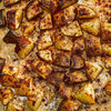 Roasted potatoes seasoned with spices are arranged on a baking sheet.