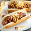 A close-up of chili dogs topped with shredded cheese and diced onions on a white plate.