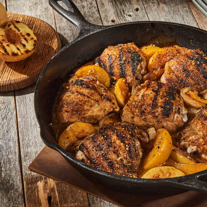 A cast iron skillet filled with grilled chicken and peaches.