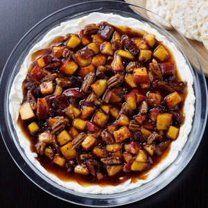 A glass dish filled with a cream cheese base topped with a sweet and savory peach and pecan topping.