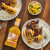 A plate of grilled chicken with black beans and rice a bowl of mango salsa and a bottle of Lawrys Cuban Style Mojo Marinade.
