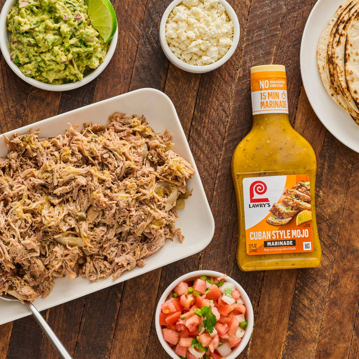 This is a shot of a table with a plate of pulled pork guacamole pico de gallo crumbled cheese tortillas and a bottle of Lawrys Cuban Style Mojo Marinade.