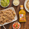 This is a shot of a table with a plate of pulled pork guacamole pico de gallo crumbled cheese tortillas and a bottle of Lawrys Cuban Style Mojo Marinade.