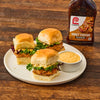 ["A plate of Lawry's Honey Teriyaki chicken sliders with a side of sauce sits on a wooden table next to a bottle of Lawry's Honey Teriyaki marinade."]