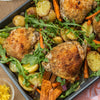 ['A close-up of a sheet pan with roasted chicken, potatoes, carrots, and arugula.']