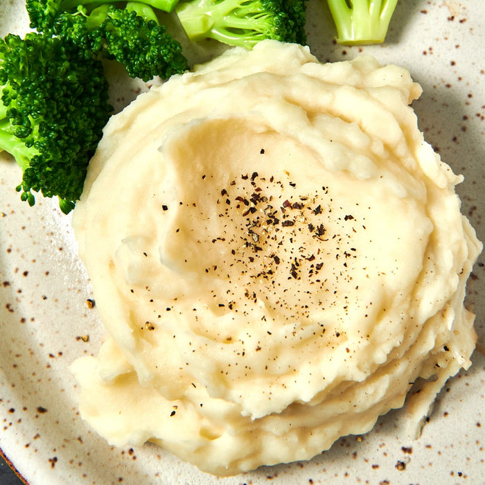 ['A plate of mashed potatoes with black pepper on top and broccoli on the side.']