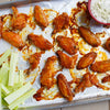 A baking sheet with chicken wings celery sticks and a bowl of blue cheese dip.