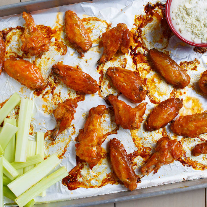 A baking sheet with chicken wings celery sticks and a bowl of blue cheese dip.