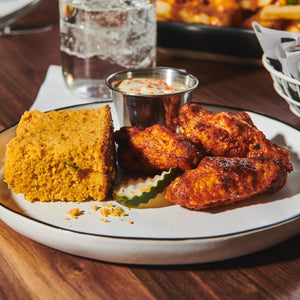 A plate of food with cornbread fried chicken wings and a pickle.