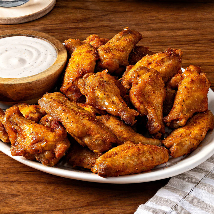 A plate of crispy chicken wings is served with a side of creamy dipping sauce, perfect for a delicious and satisfying meal.