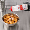 A hand in a black glove generously sprinkles Lawry'S Seasoning Salt &amp; Vinegar, 20 Oz over a stainless steel bowl full of freshly fried chicken wings.