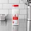 A clear shaker of Lawry'S Seasoning Salt &amp; Vinegar, 20 Oz, sits on a stainless steel countertop in a professional kitchen setting.