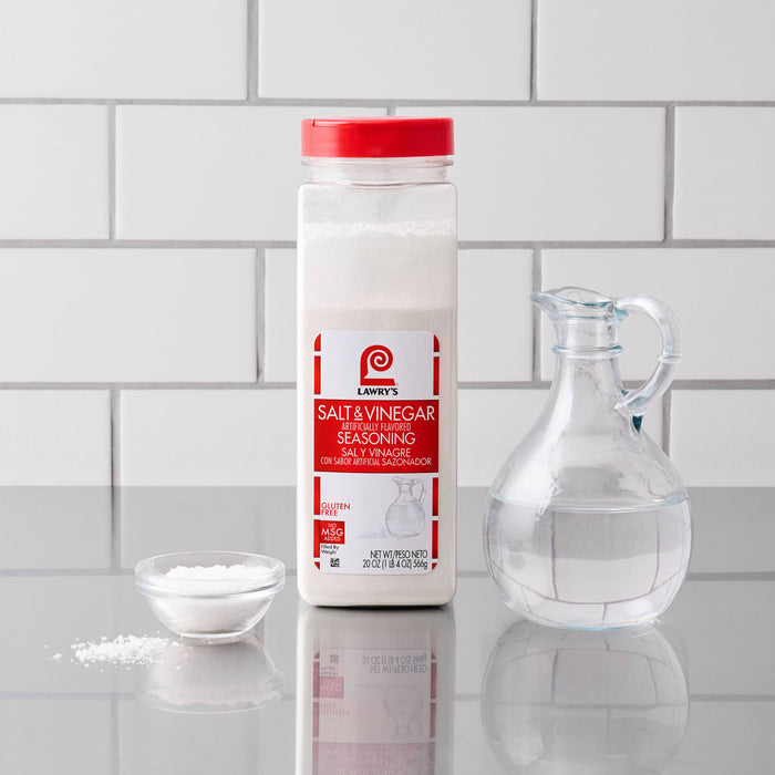 A container of Lawry'S Seasoning Salt &amp; Vinegar, 20 Oz is displayed on a countertop next to a small bowl of the seasoning and a glass cruet of vinegar.