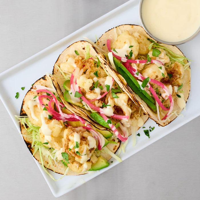 Crispy cauliflower tacos, garnished with pickled red onion and a creamy sauce, are a flavorful meal idea made with Lawry'S Seasoning Salt &amp; Vinegar, 20 Oz.
