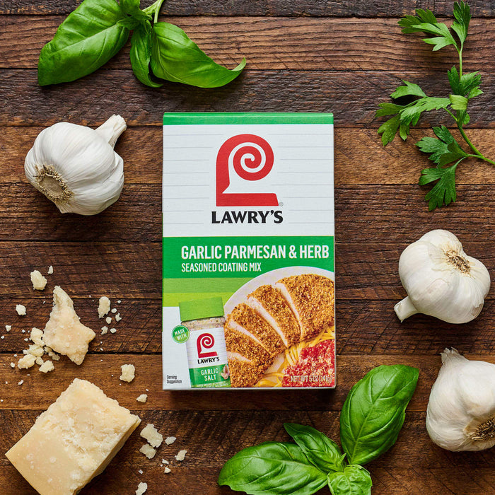 A box of Lawry's Garlic Parmesan &amp; Herb Skillet Sauce Mix is displayed with fresh garlic, basil, parsley, and parmesan cheese on a wooden surface.