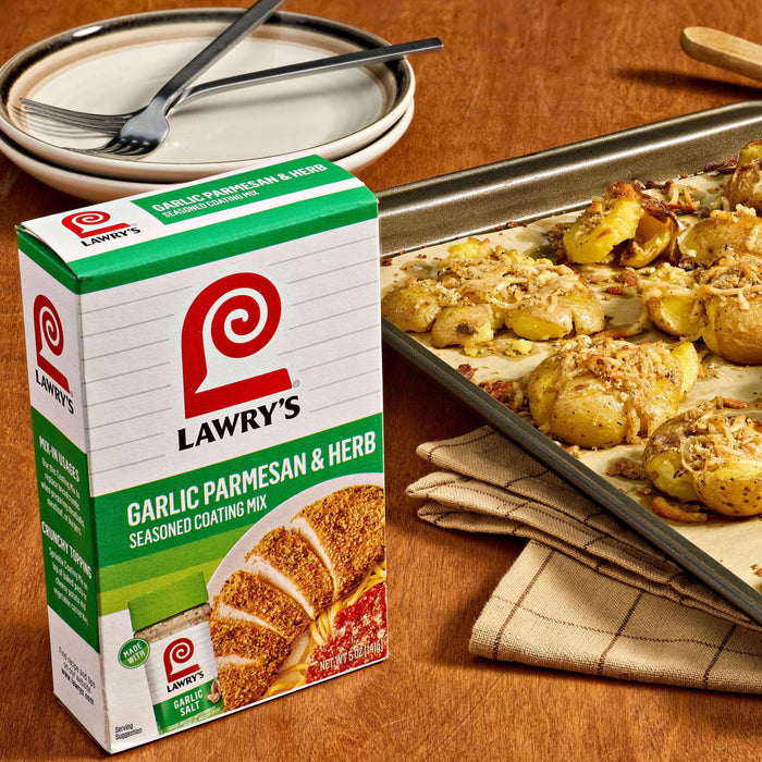 A box of Lawry's Garlic Parmesan and Herb blend sits next to a baking sheet of golden, smashed potatoes.