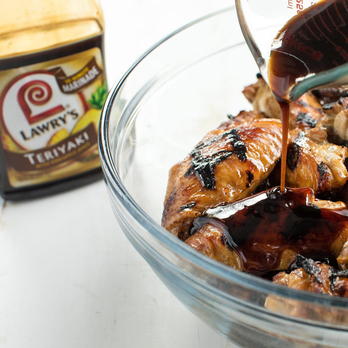 ["A glass bowl of grilled chicken being drizzled with Lawry's Teriyaki marinade."]