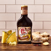 ["A bottle of Lawry's Teriyaki marinade with pineapple juice, next to pineapple slices and ginger root."]