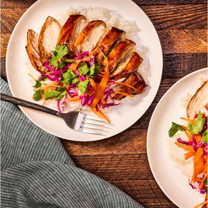 ['Two plates of chicken with rice, red cabbage, carrots, and cilantro.']