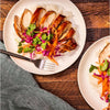 ['Two plates of chicken with rice, red cabbage, carrots, and cilantro.']
