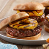 ['Three grilled pineapple burgers on a white plate.']