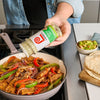 ["A hand sprinkles Lawry's Garlic Salt over a skillet of chicken and peppers."]