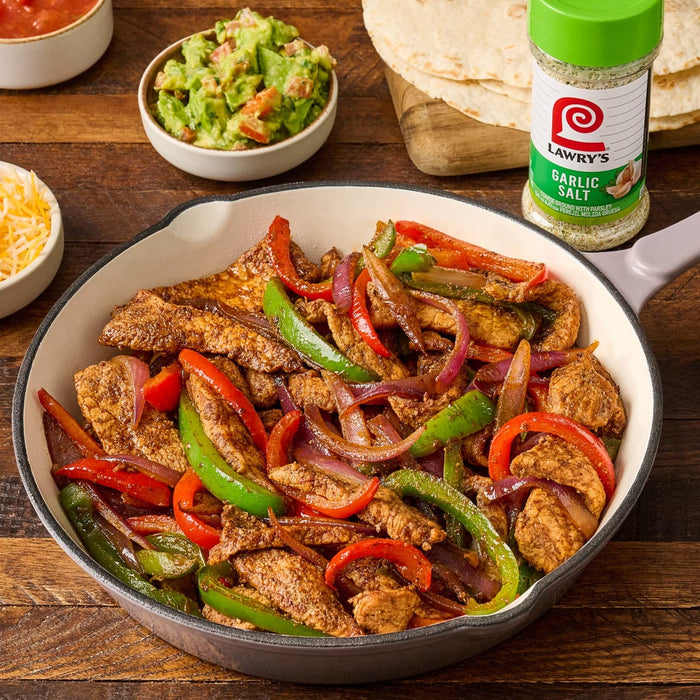 ["A skillet of Lawry's Garlic Salt seasoned chicken fajita ingredients."]