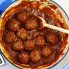 A pot of meatballs in tomato sauce with a wooden spoon.