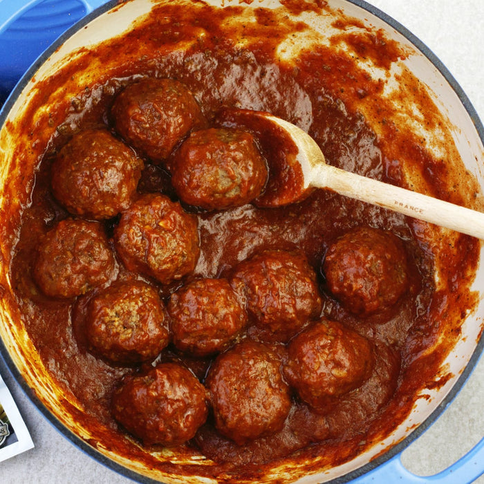 A pot of meatballs in tomato sauce with a wooden spoon.