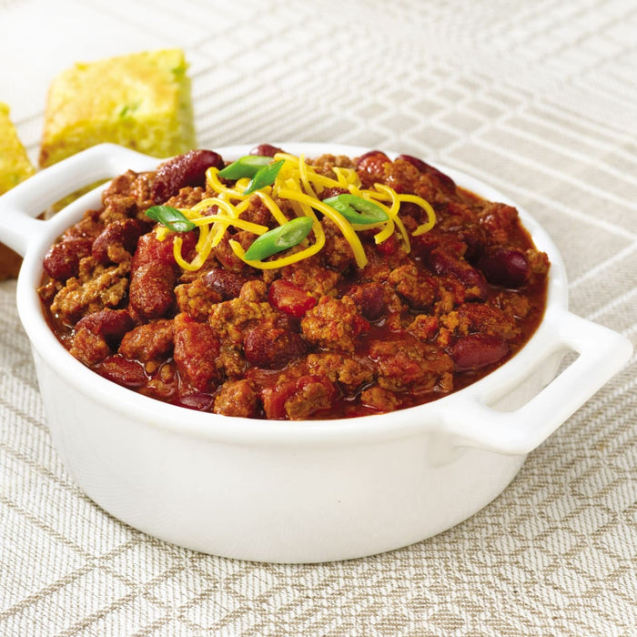 A bowl of chili with shredded cheese and green onions, served with cornbread.