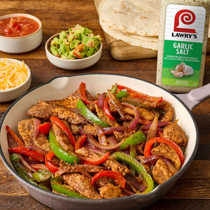 A skillet of chicken fajita ingredients seasoned with Lawrys Garlic Salt.
