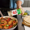 A person seasons fajitas in a pan with Lawry's Garlic Salt.