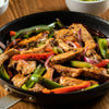 A skillet filled with sizzling fajitas featuring colorful bell peppers, red onions, and seasoned strips of meat.