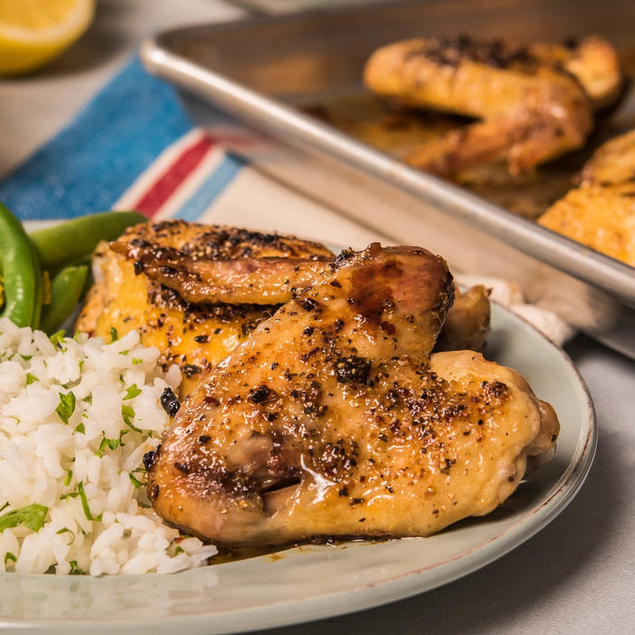 A plate of glazed chicken wings served with rice and green beans, alongside a baking sheet with more wings.