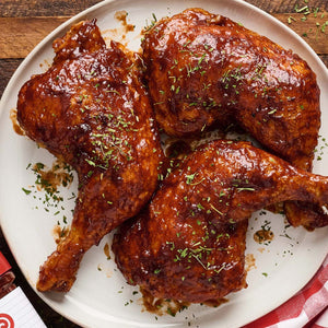 Three pieces of BBQ chicken glazed with Sweet Baby Ray's sauce are arranged on a plate, garnished with herbs.