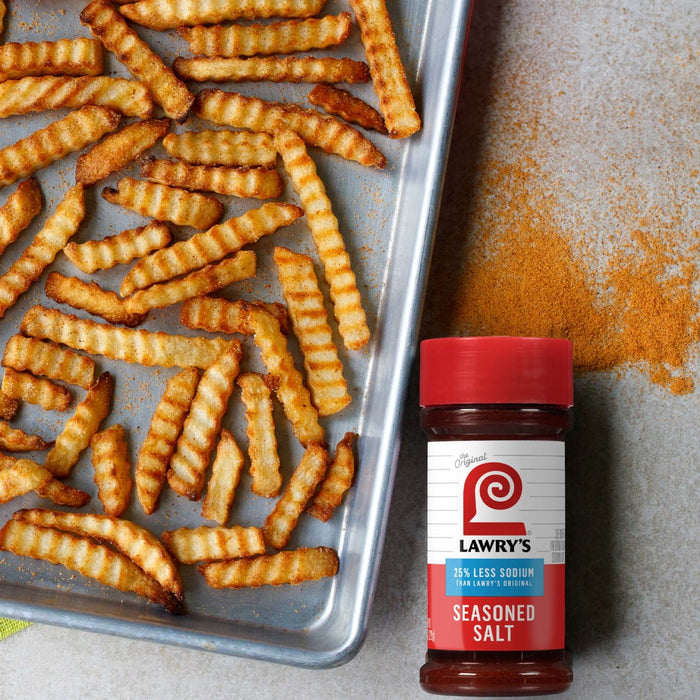 ["A tray of crispy french fries with a bottle of Lawry's Seasoned Salt."]