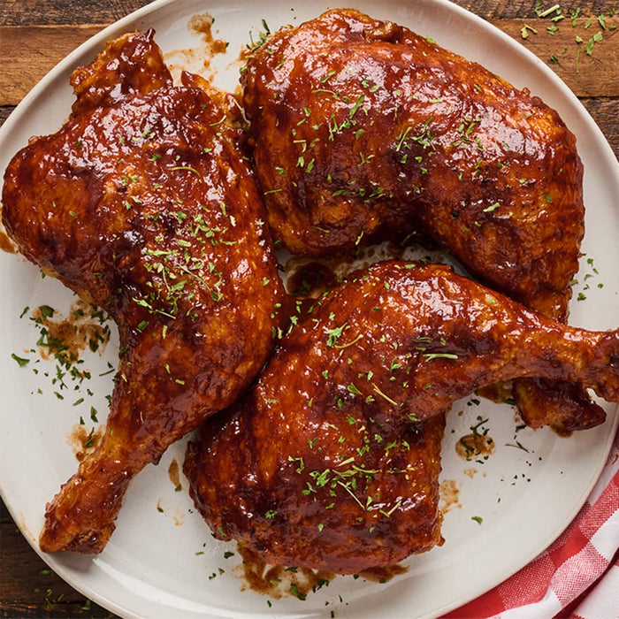 ['Three chicken legs are covered in barbecue sauce and garnished with parsley on a white plate.']