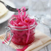 A jar of pickled red onions with a fork holding some of the onions.