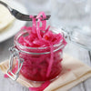 A jar of pickled red onions with a fork holding some of the onions.