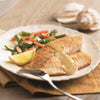 A plate of pan-fried fish with a creamy sauce served with asparagus carrots almonds and a lemon wedge.