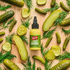 A bottle of French's Dill Pickle Mustard Spread is surrounded by pickles and dill sprigs on a wooden surface.