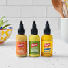 Three bottles of French's mustard in maple, dill pickle, and honey flavors are displayed on a countertop.