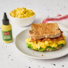 A French's Dill Pickle Mustard Spread bottle is featured next to a sandwich with egg salad, bacon, and lettuce, and a bowl of egg salad.