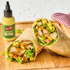 Two halves of a wrap filled with lettuce, tomatoes, chicken, and French's Dill Pickle Mustard Spread are displayed on a wooden board next to a bottle of the mustard.