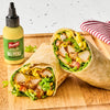 Two halves of a wrap filled with lettuce, tomatoes, chicken, and French's Dill Pickle Mustard Spread are displayed on a wooden board next to a bottle of the mustard.